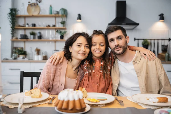 Preteen girl hugging parents near Easter dinner and cake at home — Stock Photo