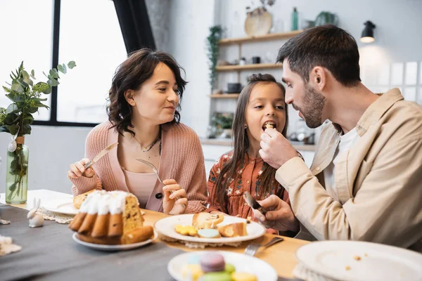 Man feeding daughter with Easter cake near wife at home — Stock Photo