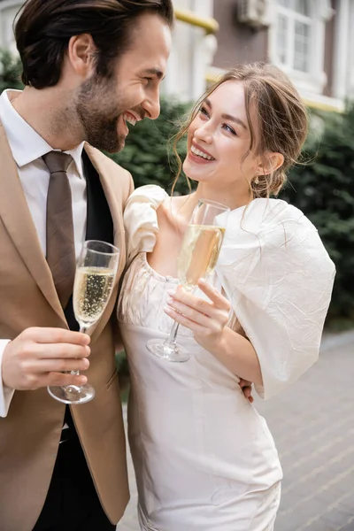 Glückliche und junge Brautpaare mit Champagnergläsern während der Hochzeitsfeier — Stockfoto