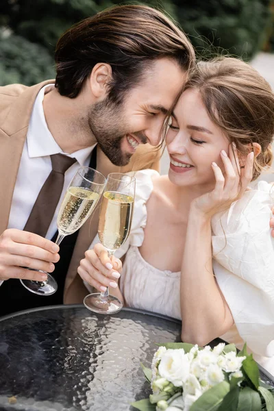 Fröhliche und junge Brautpaare mit Champagnergläsern während der Hochzeitsfeier — Stockfoto