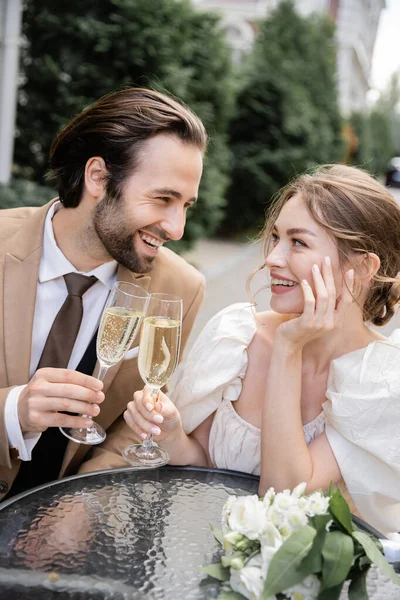 Fröhliche und junge Frischvermählte, die während der Hochzeitsfeier lächelnd Sektgläser klimpern — Stockfoto