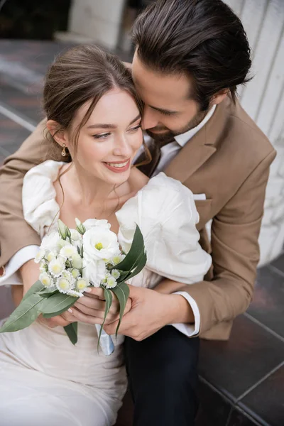 Overhead view of bearded groom hugging smiling bride in white dress with wedding bouquet — Stock Photo