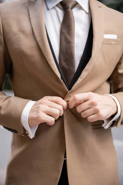 Vista recortada del hombre en camisa blanca con corbata abotonando chaqueta beige - foto de stock
