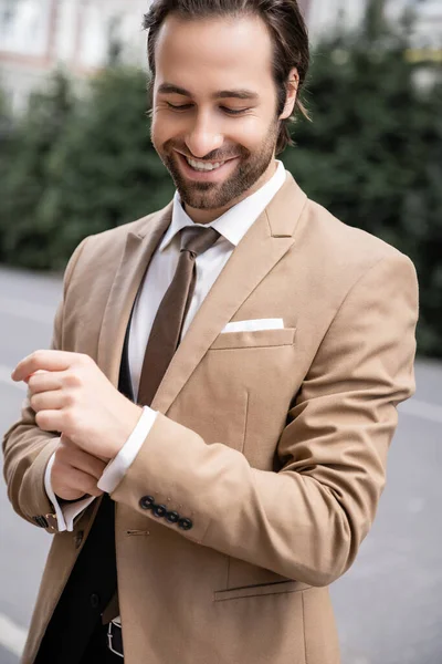 Happy groom in beige formal wear adjusting sleeve on shirt — Stock Photo