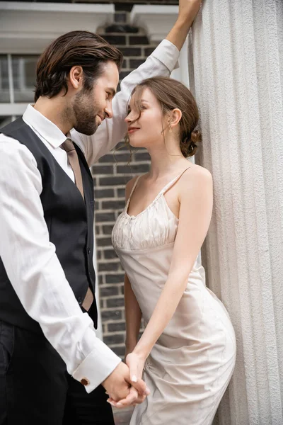 Наречений в офіційному одязі і наречена у весільній сукні тримає руки, дивлячись один на одного — стокове фото