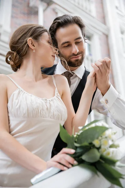 Portrait of bearded groom holding hand of bride with wedding bouquet — Foto stock