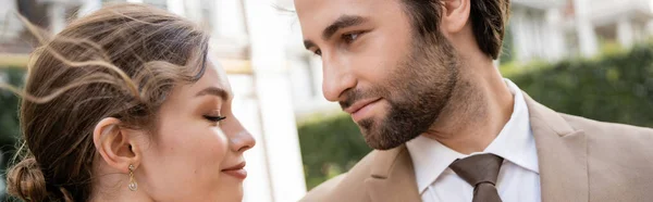 Бородатий чоловік у костюмі, дивлячись на усміхнену наречену на відкритому повітрі, банер — стокове фото