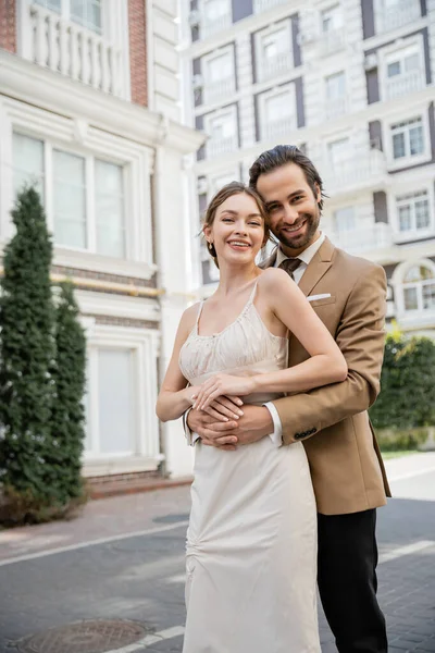 Bearded man in suit with tie smiling and hugging happy bride in wedding dress — Stock Photo