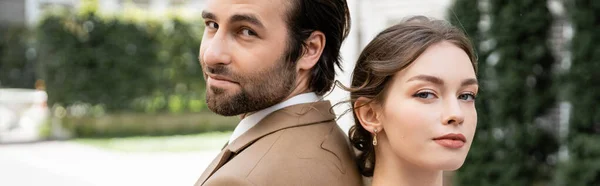 Pretty bride and groom in suit standing back to back while looking at camera, banner — Stock Photo