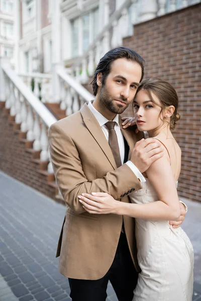 Groom in beige suit hugging sensual bride in white wedding dress — Stock Photo