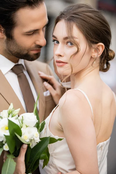 Retrato de novia en vestido de novia sosteniendo flores en flor y abrazando con el novio - foto de stock