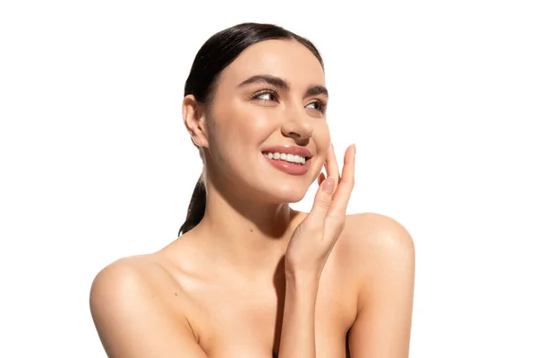 Happy young woman with natural makeup and bare shoulders touching cheek isolated on white — Stock Photo