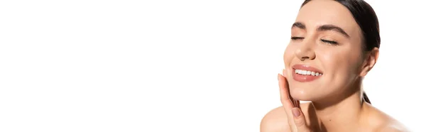 Pleased young woman with natural makeup and bare shoulders touching cheek isolated on white, banner — Stock Photo