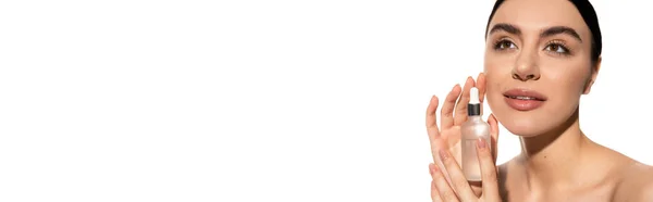 Dreamy woman with bare shoulders holding bottle with moisturizing serum isolated on white, banner — Stock Photo