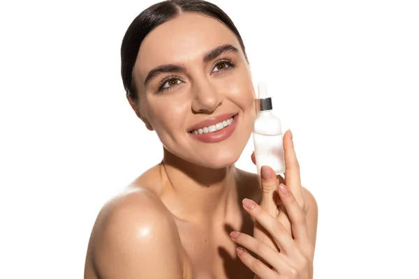 Mujer joven positiva con maquillaje natural sosteniendo la botella con suero aislado en blanco - foto de stock