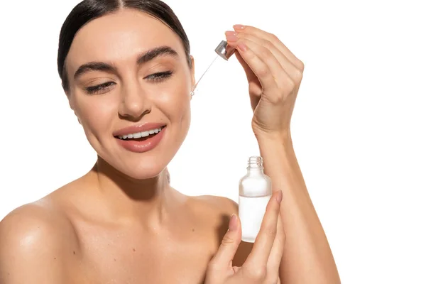 Happy young woman with bare shoulders holding pipette with vitamin c serum isolated on white — Stock Photo