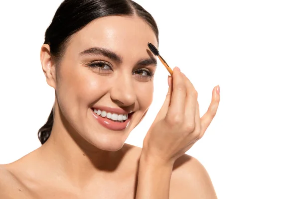 Happy and brunette woman styling eyebrows with gel isolated on white — Stock Photo