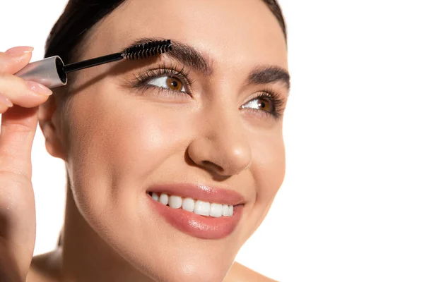 Close up of happy young woman holding brush and styling eyebrows with gel isolated on white — Photo de stock