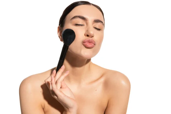 Brunette woman with bare shoulders holding soft powder brush and pouting lips isolated on white — Stock Photo