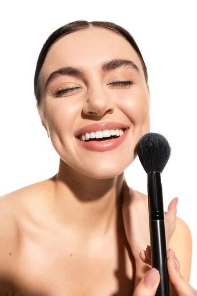 Satisfied woman with bare shoulders holding soft powder brush near face isolated on white — Photo de stock