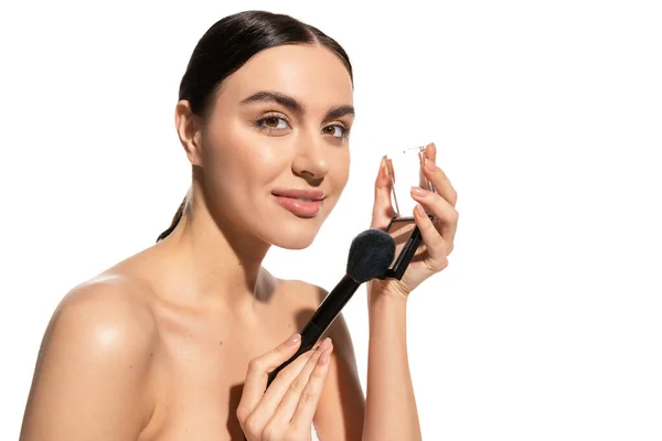 Mujer satisfecha sosteniendo cepillo cosmético suave cerca de rubor polvo aislado en blanco - foto de stock