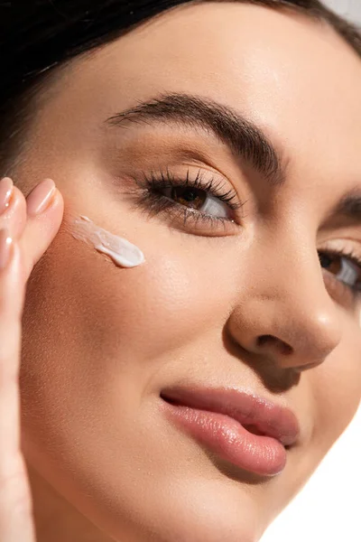 Close up view of young woman with face cream on cheek looking at camera — Stock Photo