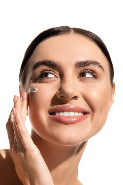 Close up view of pleased young woman with face cream on cheek looking away isolated on white — Stock Photo