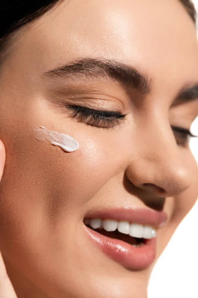 Close up view of joyful young woman with face cream on cheek isolated on white — Stock Photo