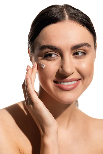 Sorrindo jovem aplicando creme facial na bochecha isolado no branco — Fotografia de Stock