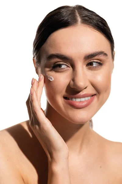 Smiling young woman applying face cream on cheek isolated on white — Stock Photo