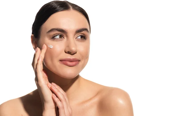 Brunette young woman applying moisturizing face cream on cheek isolated on white — Stock Photo