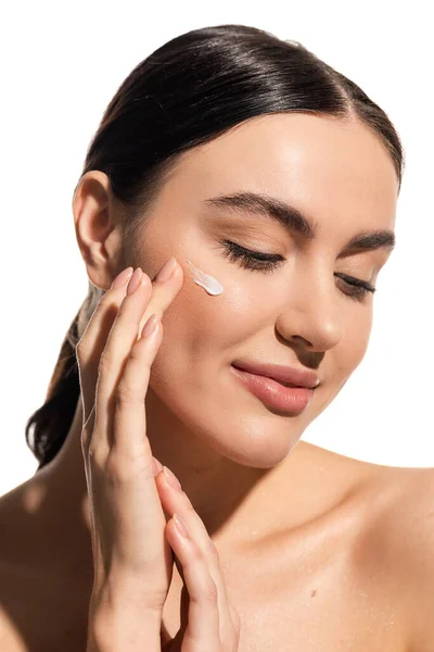 Smiling woman applying moisturizing face cream on cheek isolated on white — Stock Photo