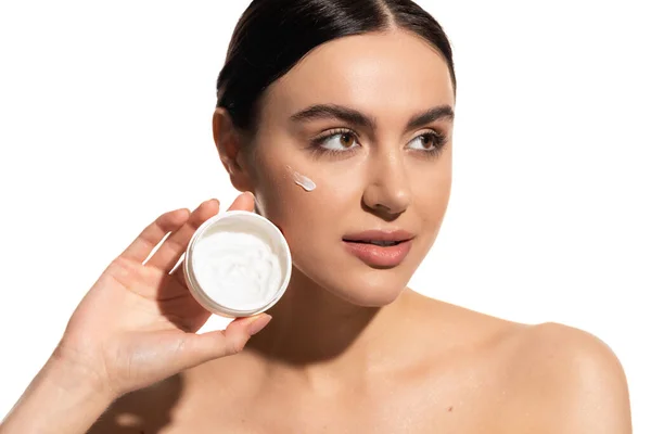Brunette woman with bare shoulders holding jar with moisturizing face cream isolated on white — Stock Photo