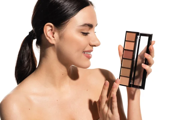 Positive young woman with bare shoulders holding eye shadow palette isolated on white — Stock Photo