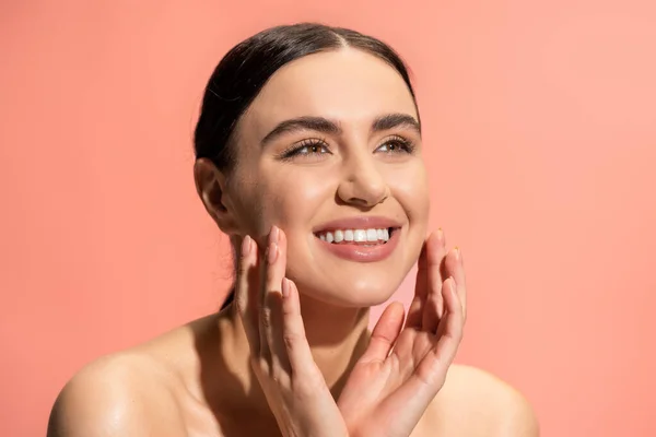 Щаслива молода жінка з голими плечима, що торкається м'яких щік ізольована на рожевому — стокове фото