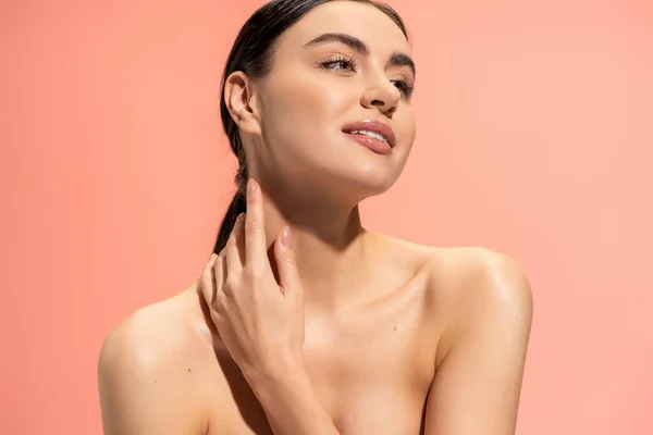 Pleased woman with bare shoulders and flawless makeup touching soft skin isolated on pink — Foto stock
