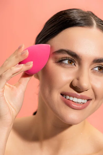 Весела молода жінка наносить макіяж фон з красивою губкою ізольовані на рожевому — стокове фото