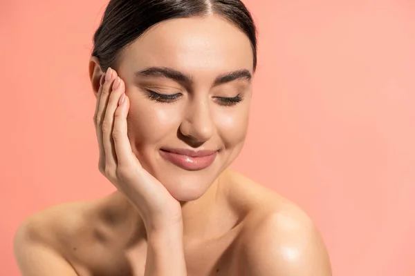 Pleased woman with naked shoulders touching soft cheek while looking away isolated on pink — Stock Photo