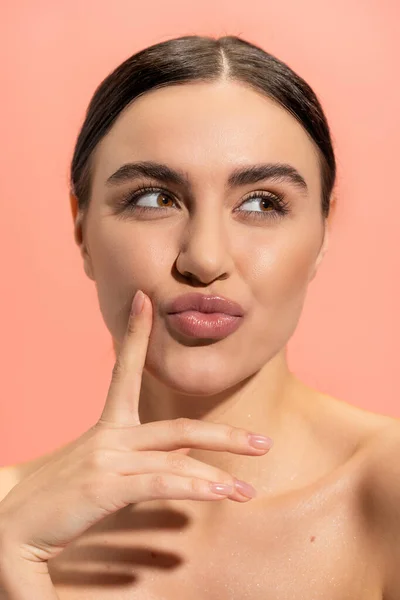 Young and brunette woman with bare shoulders pouting lips and looking away isolated on pink — Stock Photo