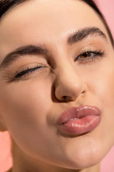 Close up of young woman pouting lips and winking eye isolated on pink - foto de stock