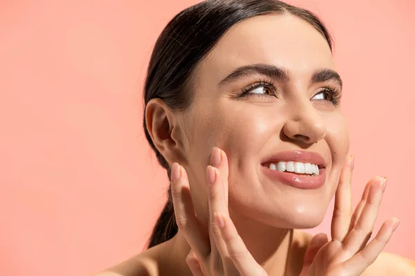 Fröhliche junge Frau berührt Wangen und blickt isoliert auf rosa — Stock Photo