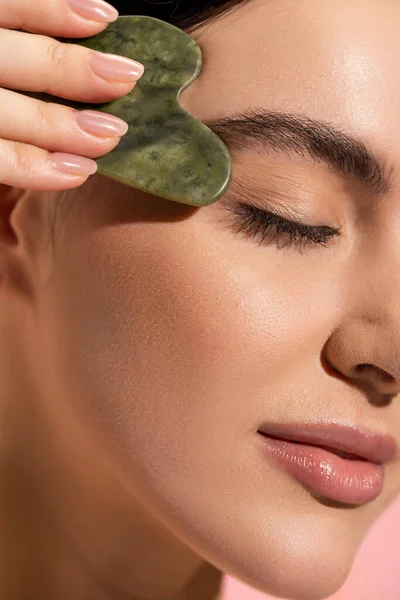 Vue rapprochée de la jeune femme à la peau douce faisant massage du visage avec grattoir de jade — Photo de stock