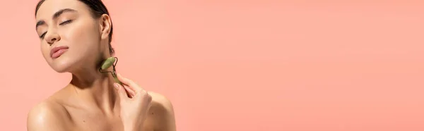 Brunette young woman doing neck massage with jade roller isolated on pink, banner — Stock Photo