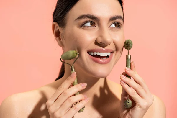 Jovem feliz fazendo massagem facial com rolos de jade isolados em rosa — Fotografia de Stock