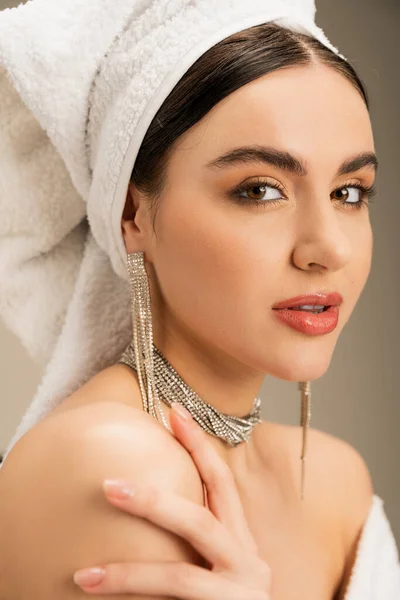 Jeune femme avec maquillage et serviette sur la tête regardant la caméra sur fond gris — Photo de stock