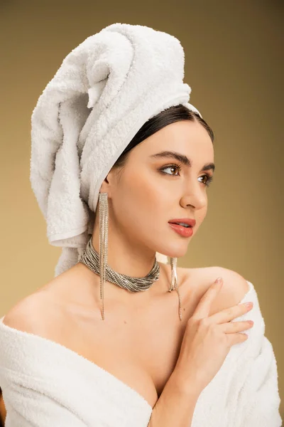 Young woman in jewelry with white towel on head looking away on beige background — Stock Photo