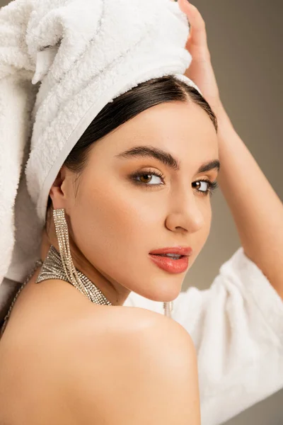 Brunette woman with makeup touching white towel on head on grey background — Stock Photo