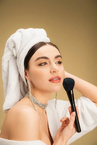 Charming woman in white towel on head applying face powder with makeup brush on beige background — Stock Photo