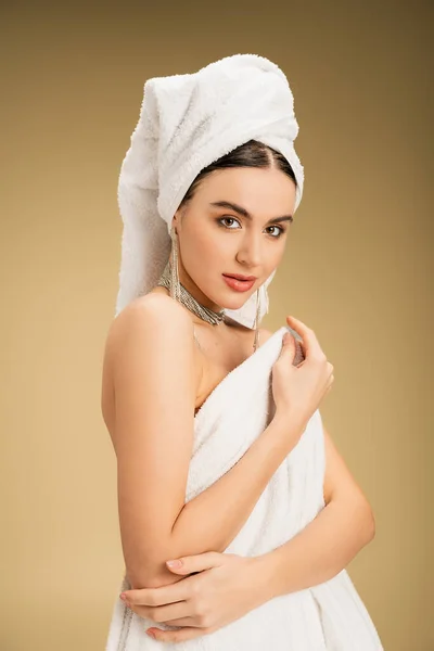 Mulher encantadora em jóias segurando toalha branca no fundo bege — Fotografia de Stock