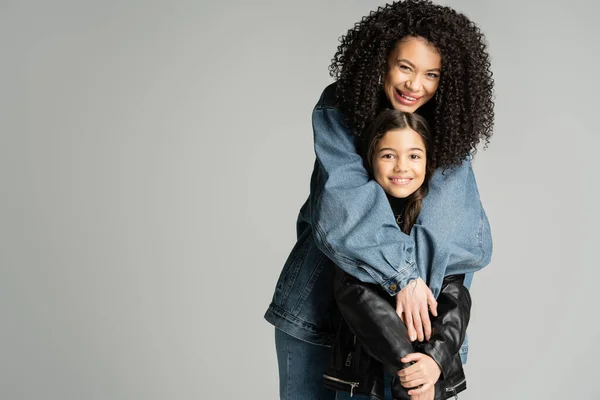 Happy curly mother hugging stylish kid in leather jacket isolated on grey — Foto stock